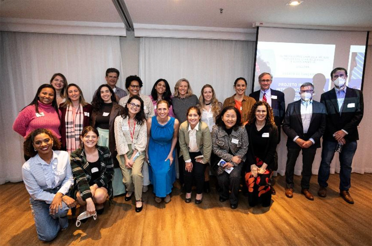 Grupo de pessoas posa para a foto, próximas a uma parede. Elas estão divididas em três grupos paralelos. São homens e mulheres, vestidos formalmente (a maioria com camisas de manga, alguns com blazer)