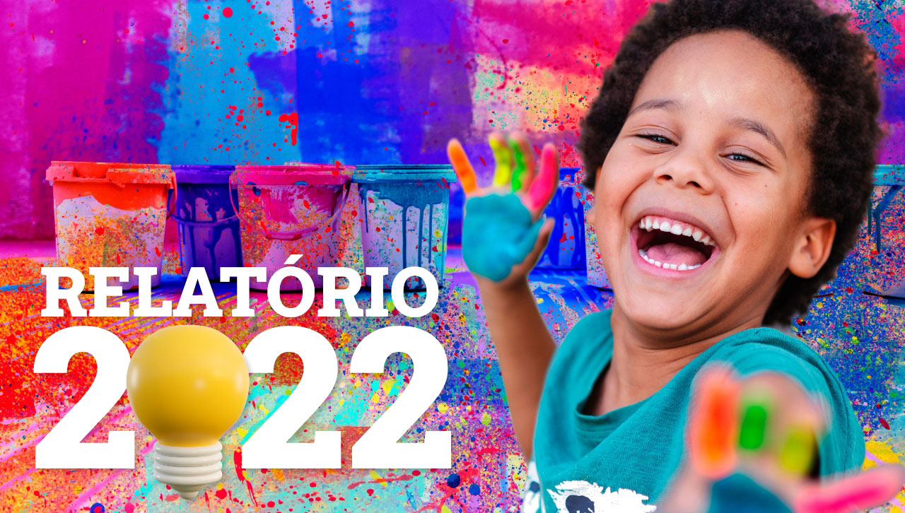 Garoto de cabelo crespo dando risada. Ele está um pouco de lado, com uma das mãos para trás, levantada, e a outra esticada na direção de quem vê a foto. As duas mãos estão com várias cores de tinta. Ele está diante de um muro todo coberto por respingos de tinta de várias cores — azul-escuro, azul-claro, rosa, vermelho, amarelo, laranja... Sobre uma parte do muro há três baldes de tinta, também inteiramente cobertos de pingos e de tinta transbordada. Sobre a imagem está escrito: Relatório 2022 — e o “0” do 2022 é uma lâmpada amarela.