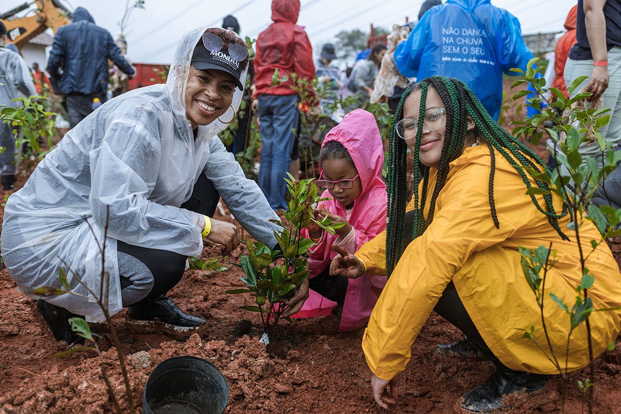 Conjunto de fotos mostra diferentes cenas da ação voluntária Viagem Fantástica: crianças, vestidas com capa de chuva, plantando mudas de árvores, lideranças falando ao microfone e grupo de pessoas reunidas num corredor.