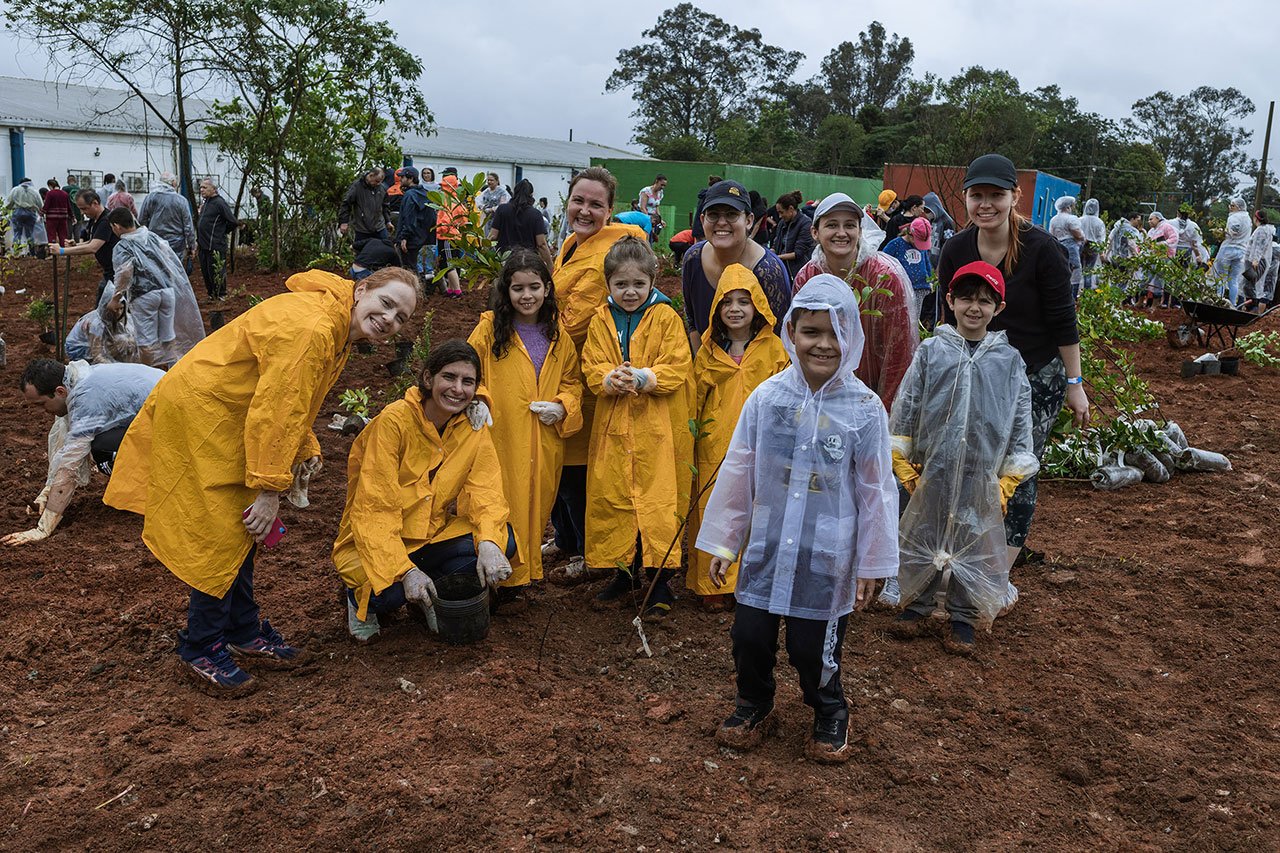 Conjunto de fotos mostra diferentes cenas da ação voluntária Viagem Fantástica: crianças, vestidas com capa de chuva, plantando mudas de árvores, lideranças falando ao microfone e grupo de pessoas reunidas num corredor.