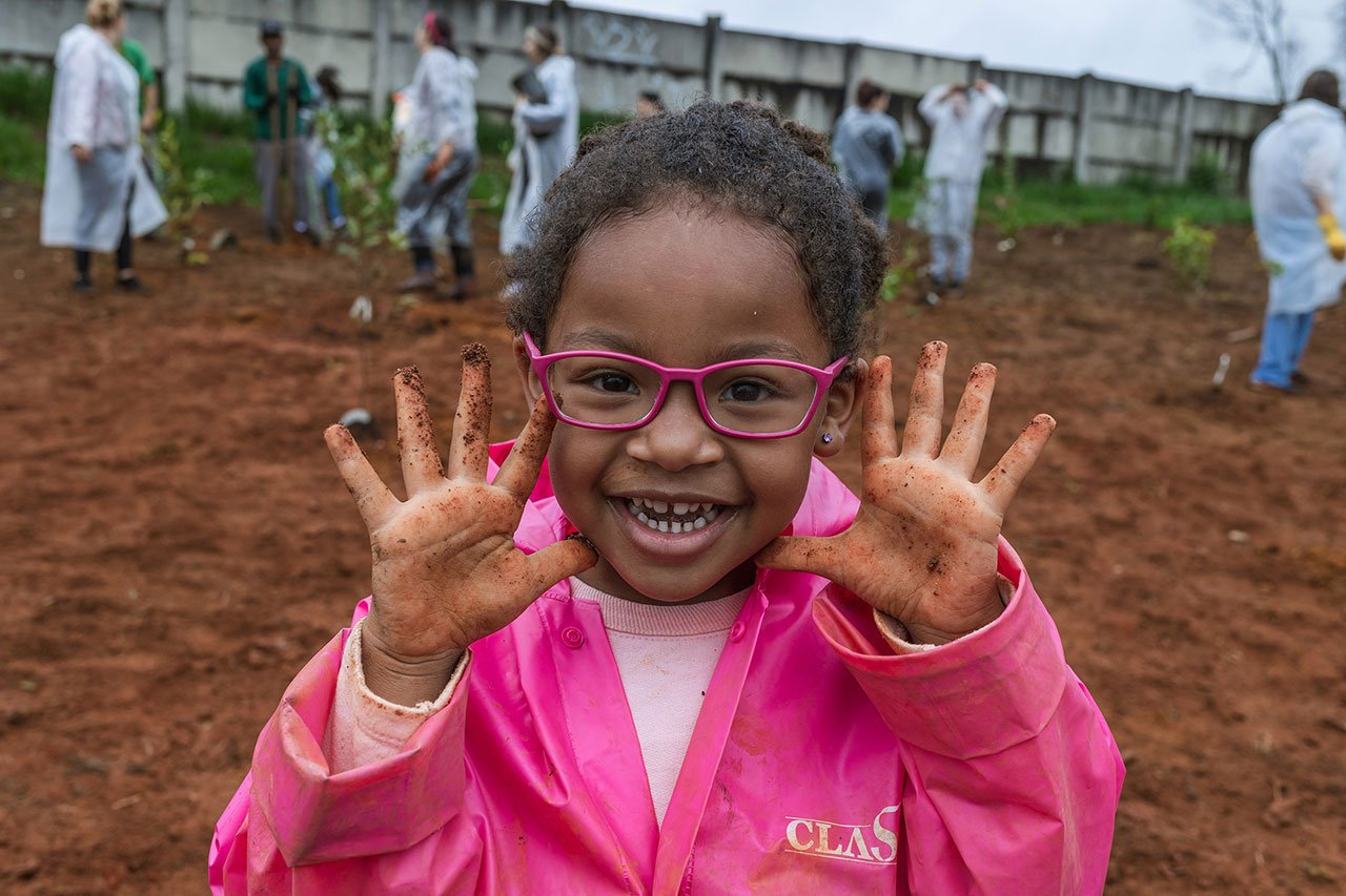 Conjunto de fotos mostra diferentes cenas da ação voluntária Viagem Fantástica: crianças, vestidas com capa de chuva, plantando mudas de árvores, lideranças falando ao microfone e grupo de pessoas reunidas num corredor.