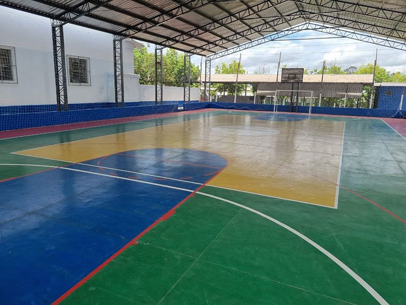 Foto de uma quadra poliesportiva coberta. No piso da quadra há linhas e marcações para basquete, vôlei e futsal.