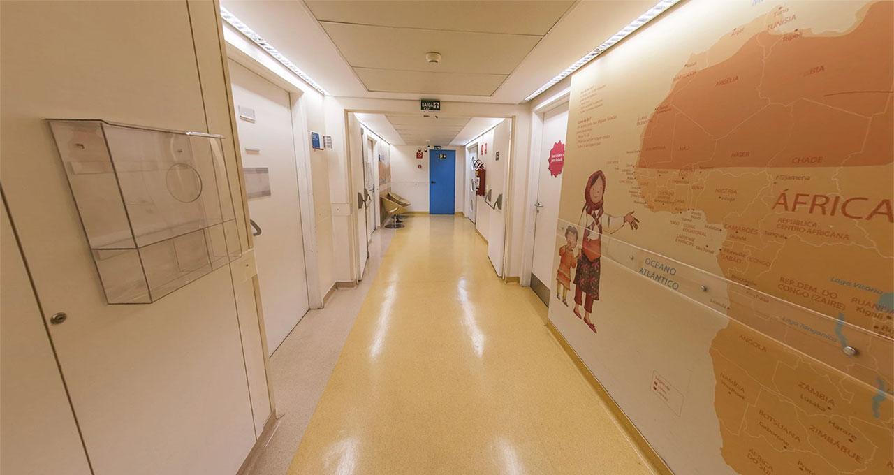 Foto de um corredor hospitalar, com piso bege. A primeira parte da parede do lado direito tem um grande mapa da África, em marrom escuro e marrom claro