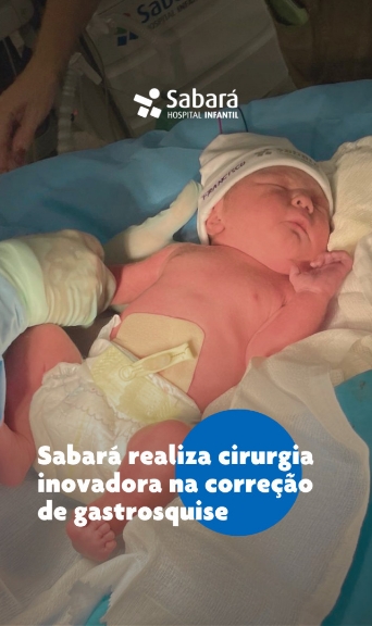 Foto de bebê deitado sobre um pano branco. Ele está com um gorro branco, sem camisa e de fralda branca, com um curativo sobre a barriga